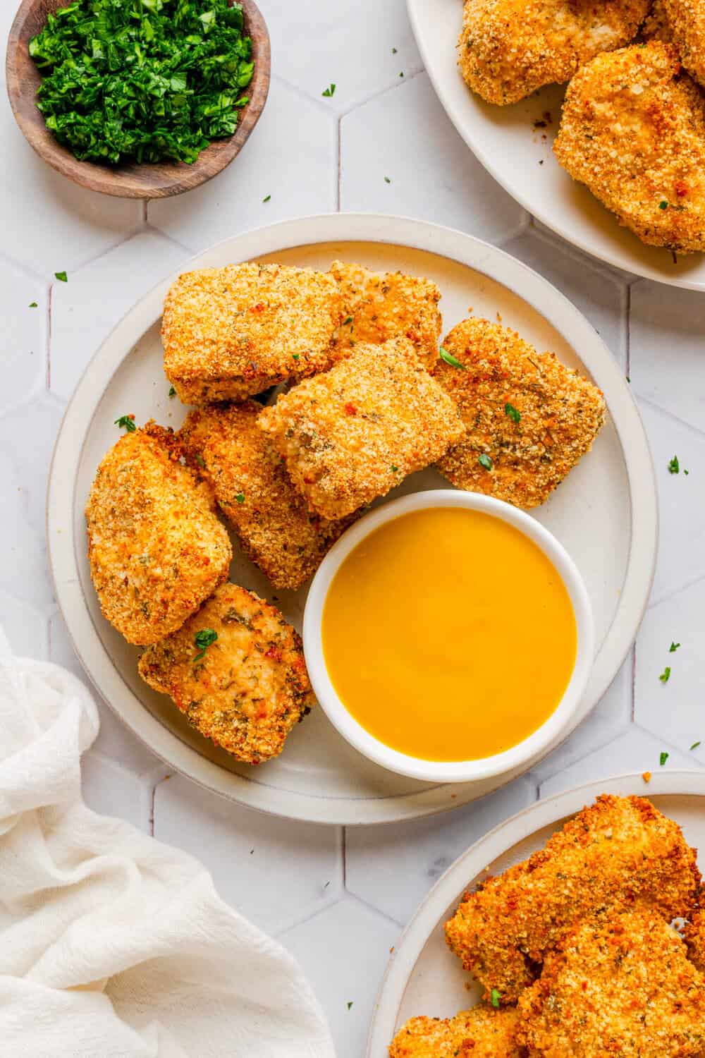 Plate filled with air fryer chicken nuggets with a bowl of honey mustard sauce on the plate and more chicken nuggets behind it. 