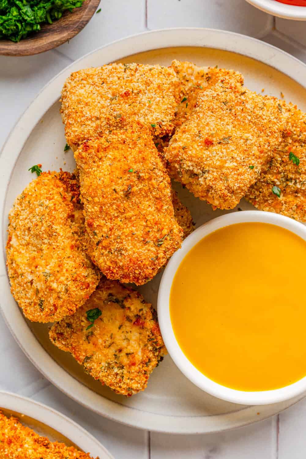 Golden healthy nuggets of chicken on a plate with yellow sauce with more in front of it. 