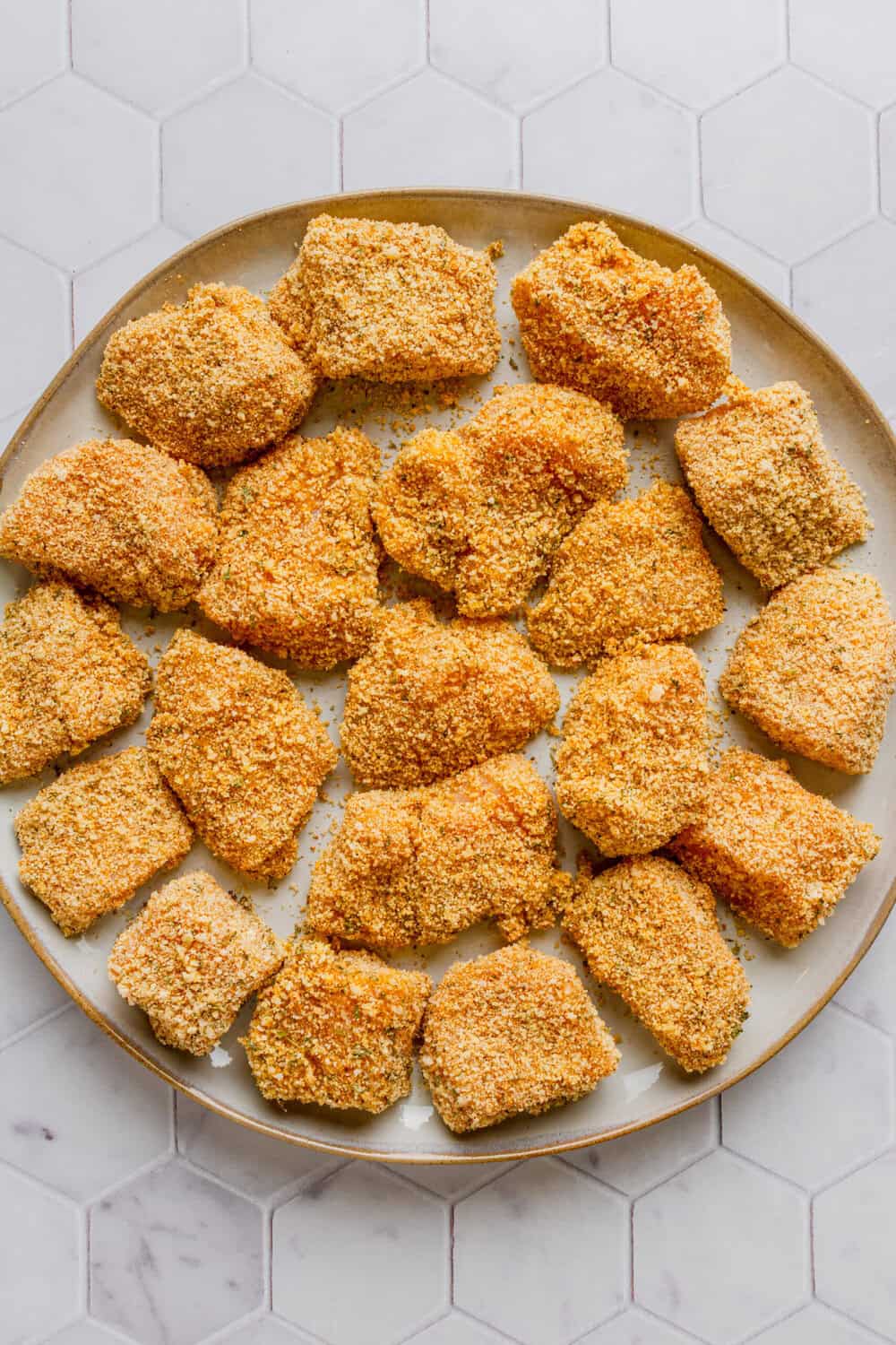Plate of uncooked breaded chicken chunks. 