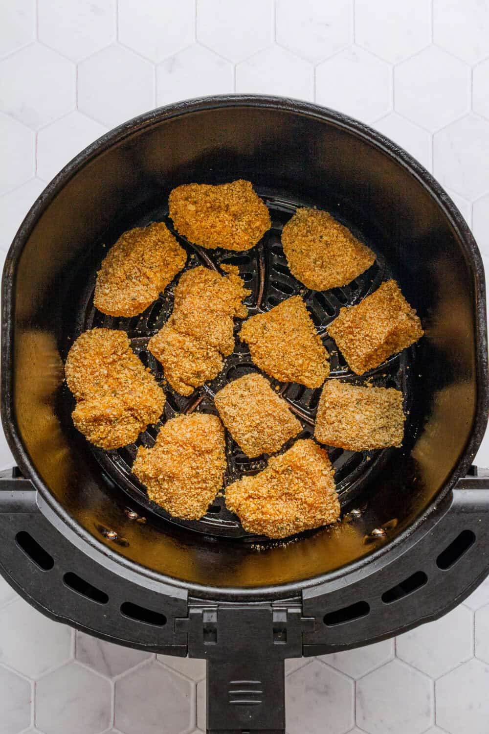 Breaded uncooked chicken chunks in an air fryer basket. 