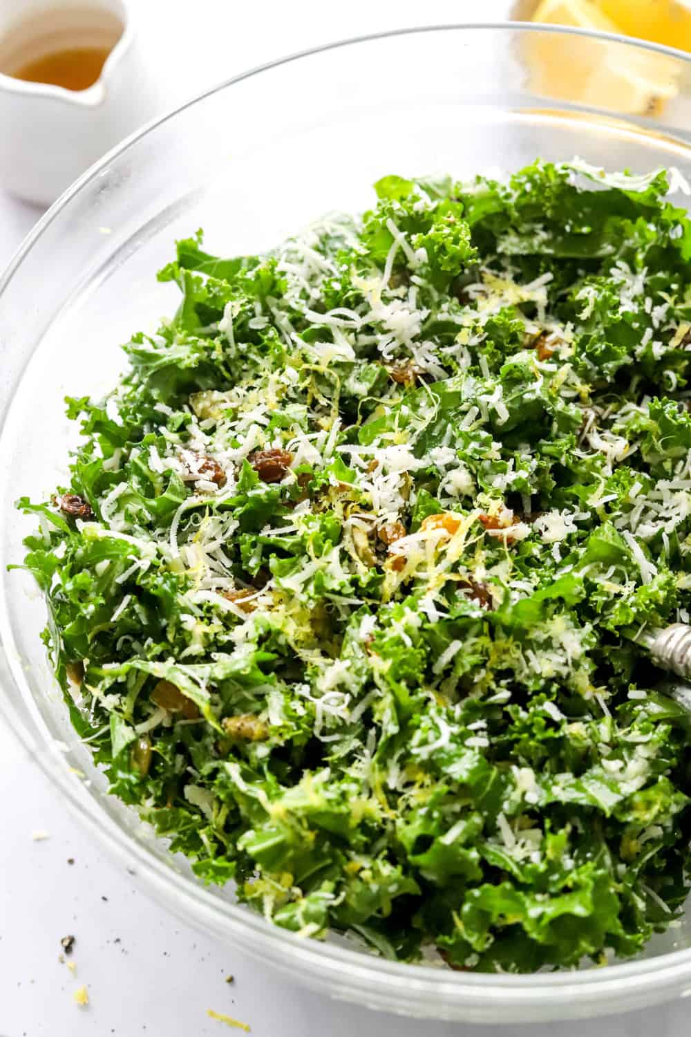 Chopped kale greens in a glass salad bowl topped with shredded cheese, lemon zest and nuts