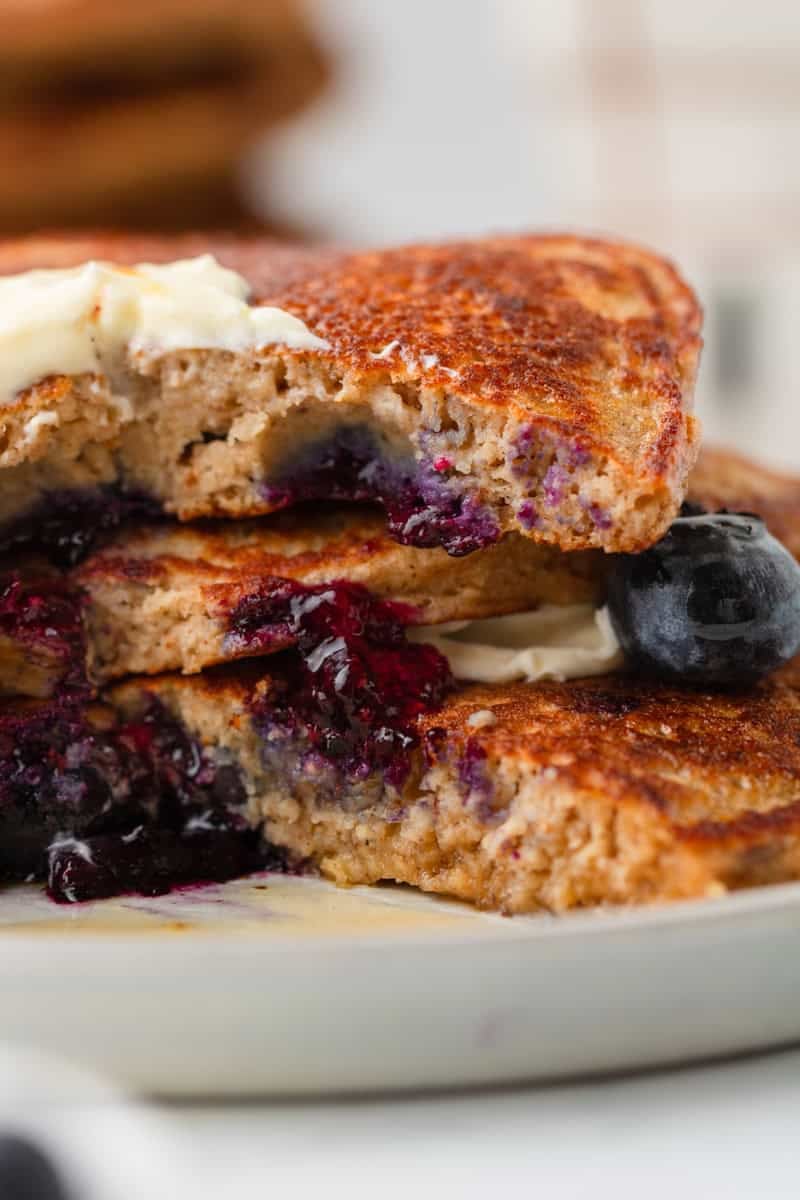 Stacked blueberry pancakes with protein powder with syrup and butter on them and a cut out of the stack of pancakes. 