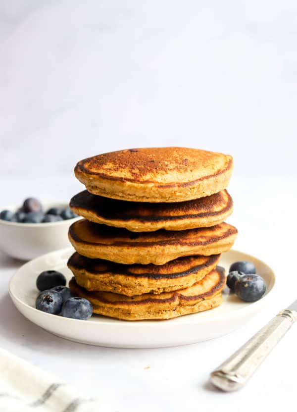 Stack or golden brown pancakes on a round, white plate with blueberries around the bottom of the plate.