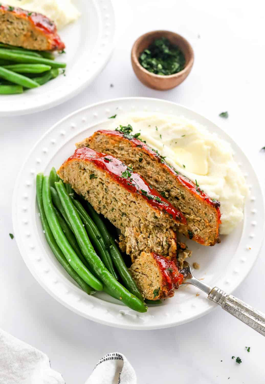 Air fried meatloaf sliced on a plate with green beans and mashed potatoes with a fork cutting through the meatloaf. 