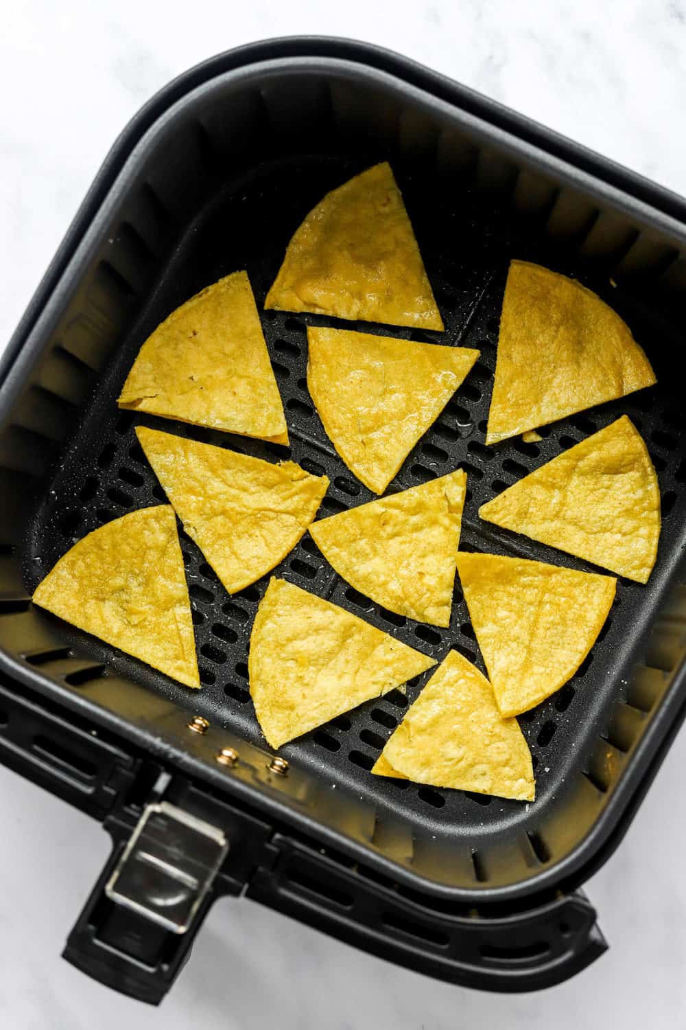 Uncooked triangle shaped tortilla pieces in a black, square air fryer basket.