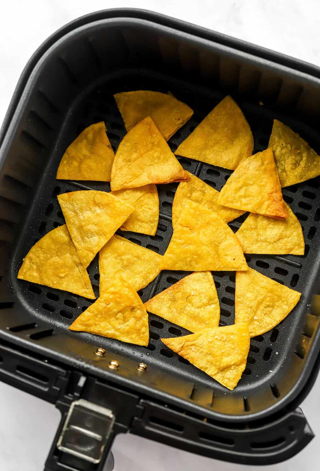 Cooked tortilla chips in a square, black air fryer basket.