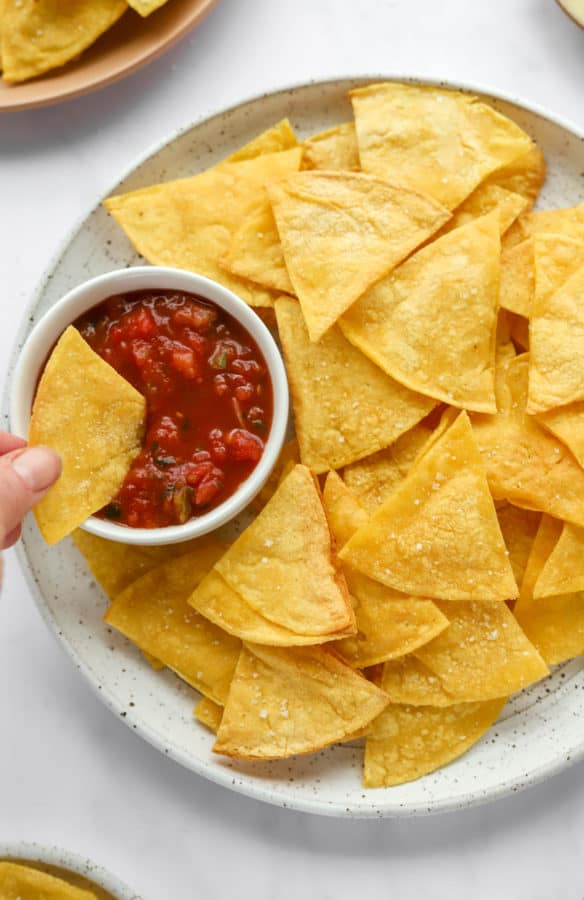 Hand dipping a tortilla chip in a white dish filled with tomato salsa.