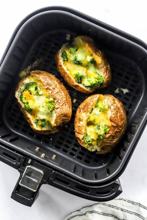 Cooked, whole potatoes filled with broccoli and melty cheddar cheese in a black air Freyr basket.