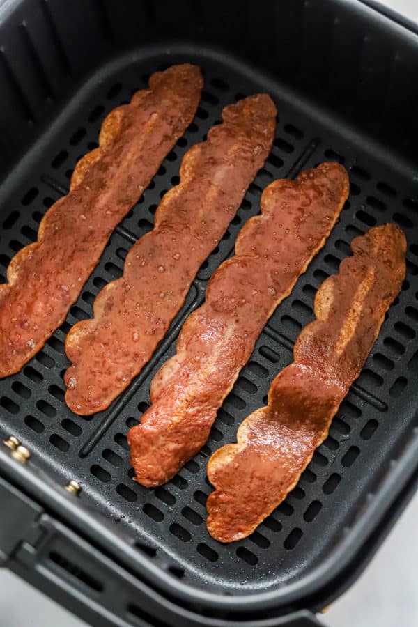 Crispy cooked bacon in a black air fryer basket.