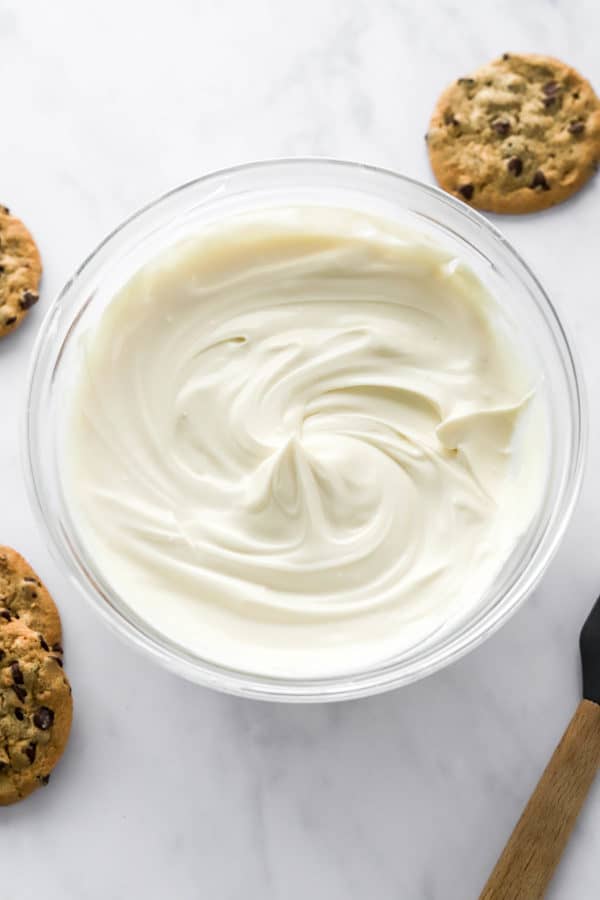 Fluffy white cream cheese frosting in a glass bowl with cookies around it.