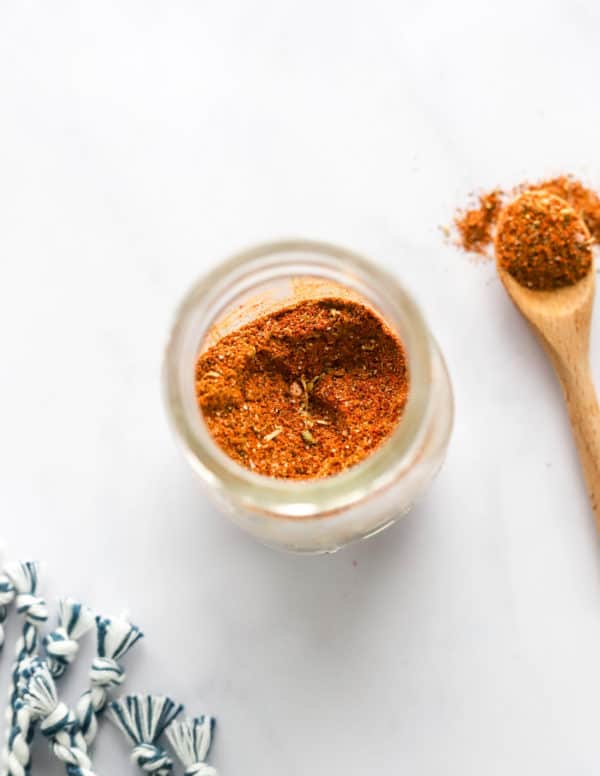 Spice blend in a small glass jar with a spoon filled with the seasoning next to it.