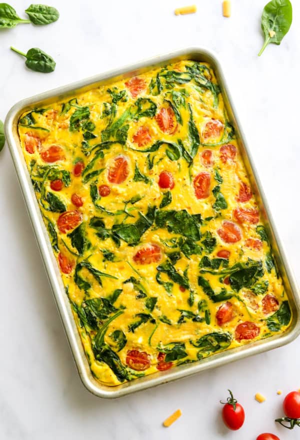 Cooked eggs with spinach and tomatoes on a baking sheet.