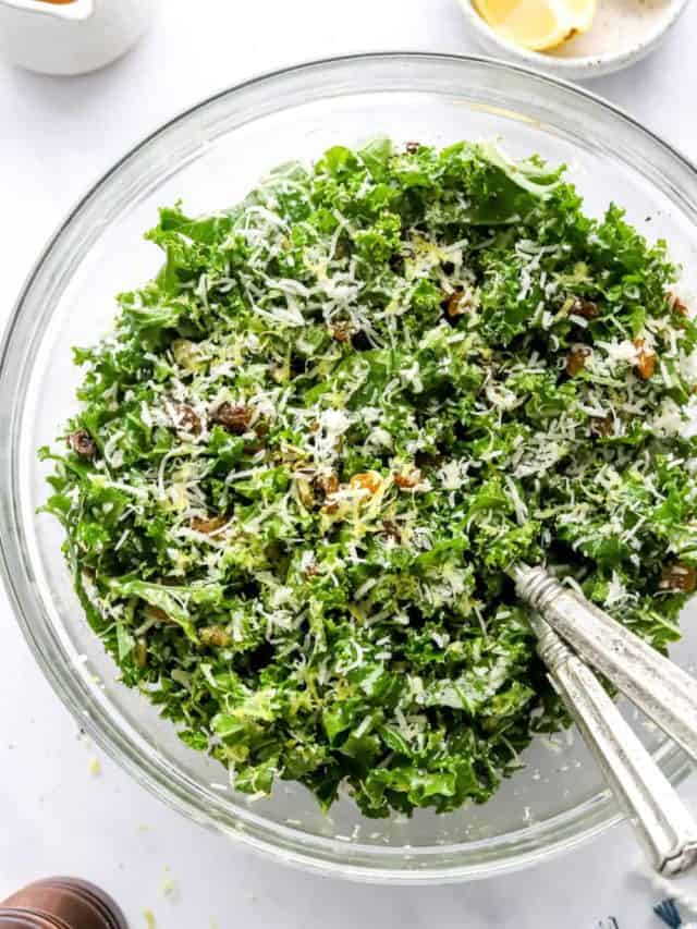 Mixed green kale salad in a bowl topped with shredded parmesan and nuts. 