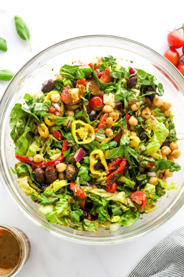 Romain lettuce mixed with olives, peppers and chickpeas in a glass bowl.