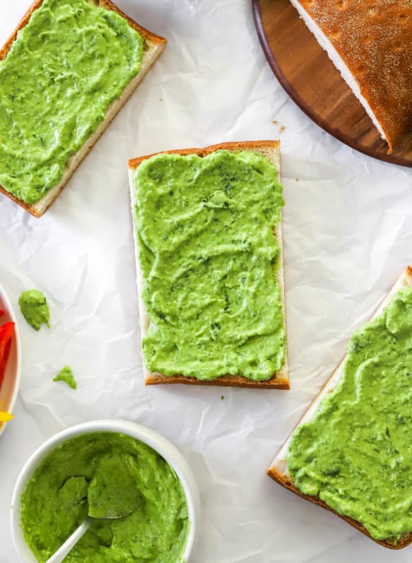 Piece of bread with green dressing spread on it with more pieces of bread with green dressing around it.