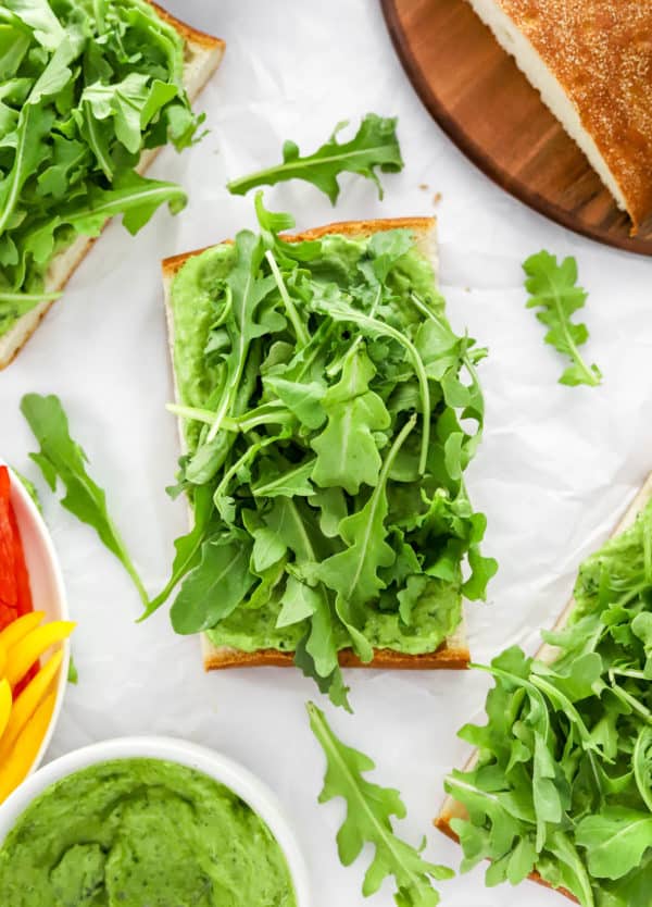 Piece of bread topped with green sauce and arugula with more around it.