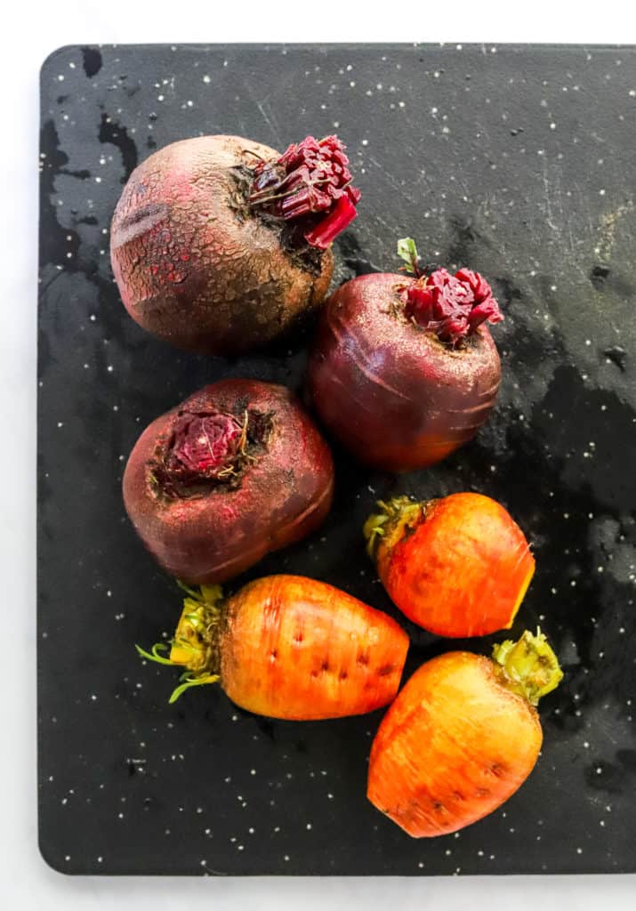 Whole red and yellow beets with greens cut off on a black cutting board.