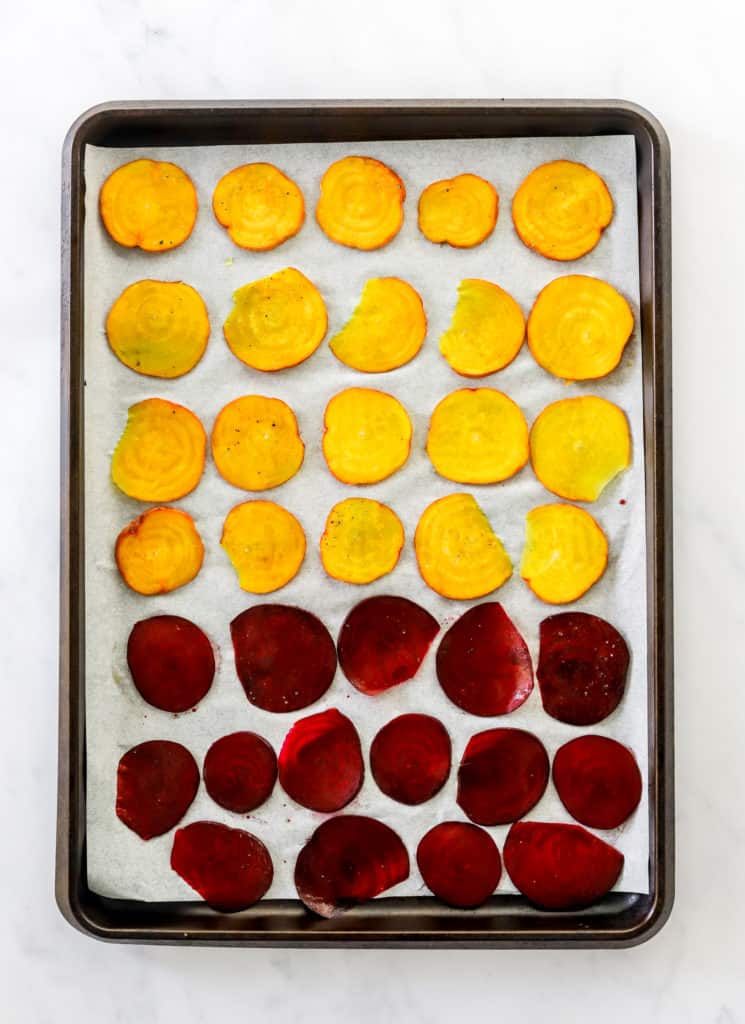 Sliced gold and red beet chips on a white parchment lined baking sheet.