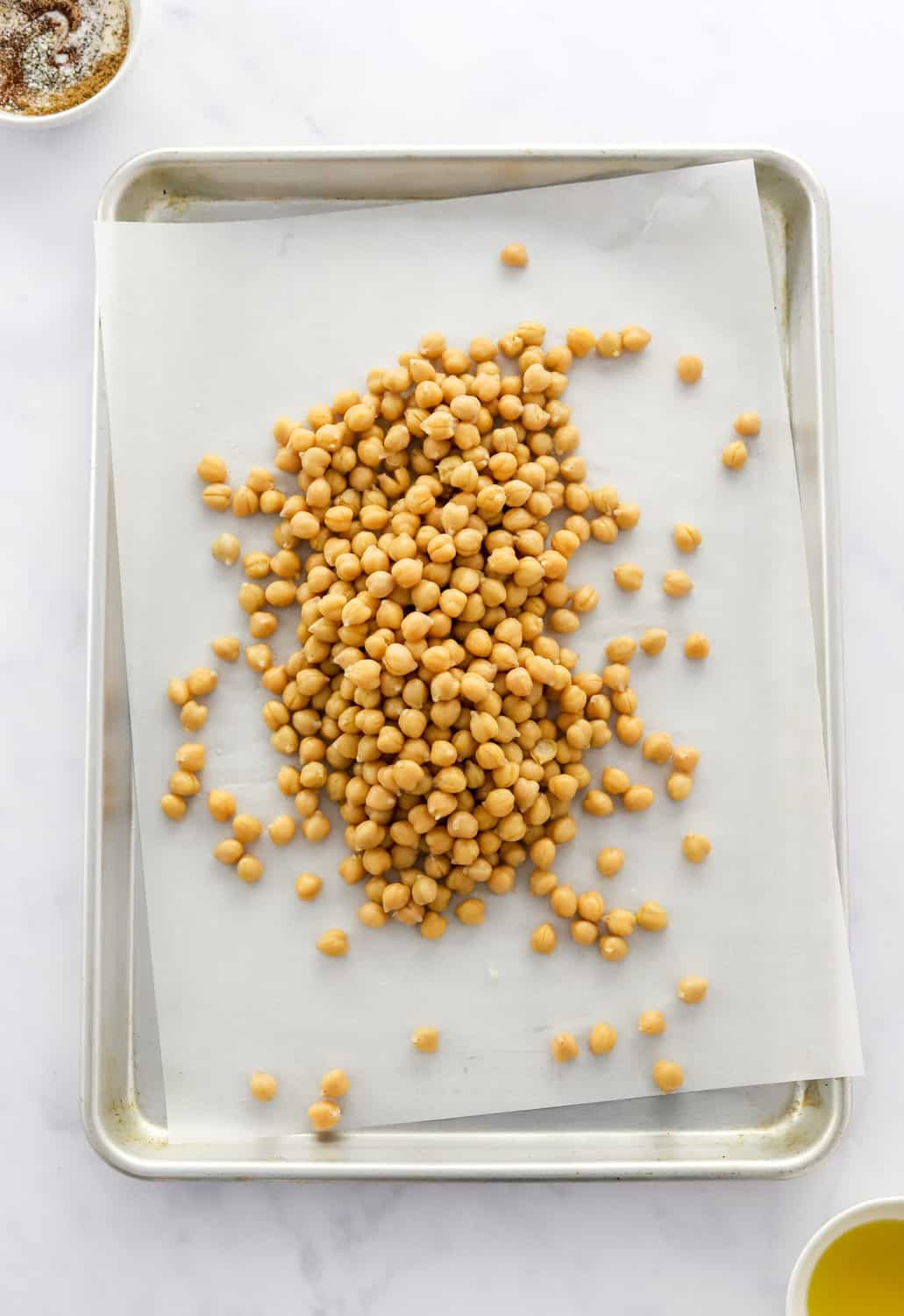 Raw chickpeas on a baking sheet on top of white parchment paper