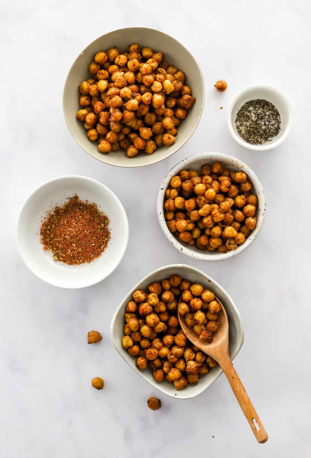 3 bowls filled with roasted chickpeas with a bowl of spices and a bowl of salt and pepper next to them. 