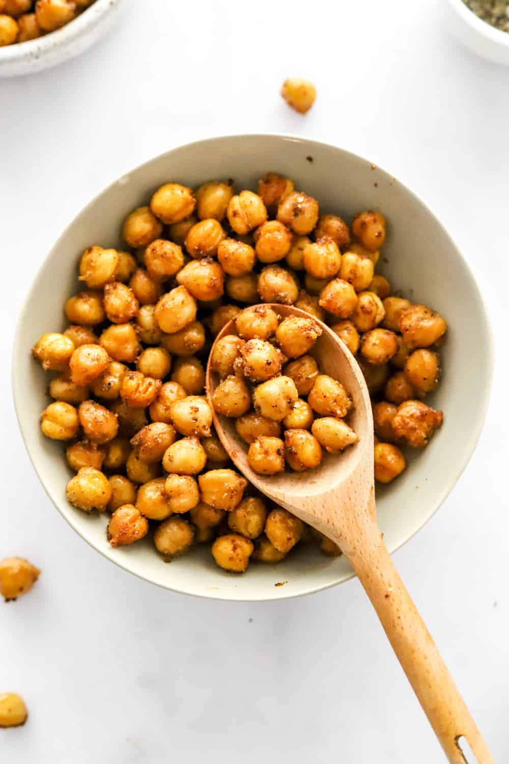 Round white bowl filled with crunchy golden chickpeas with a wooden spoon in the bowl. 