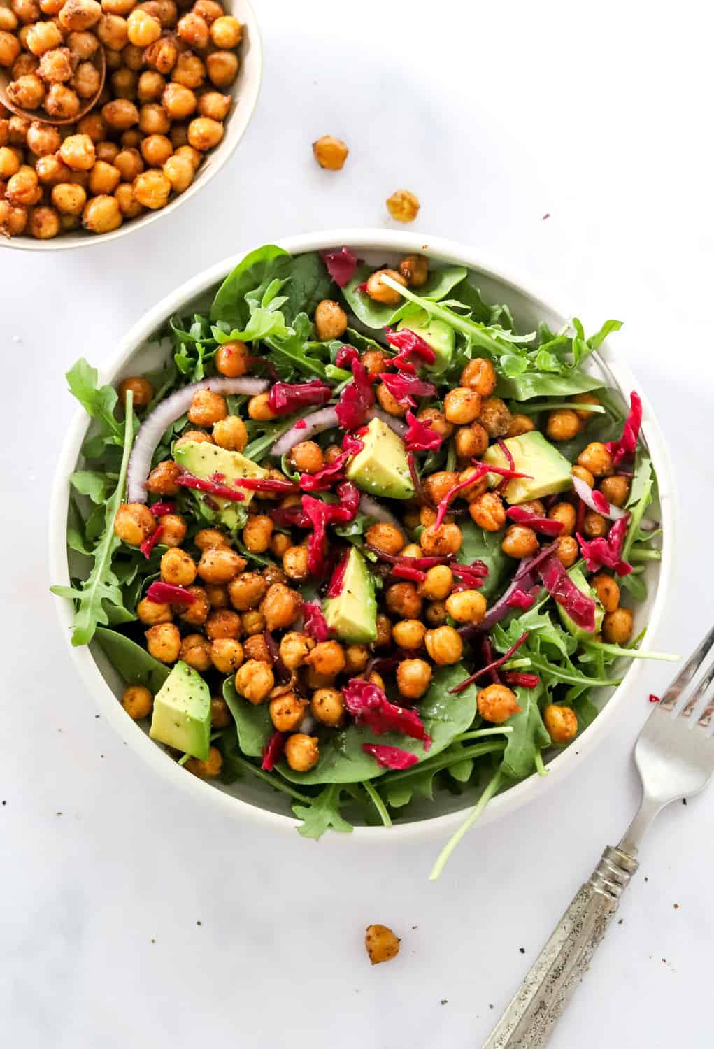 Round bowl filled with greens, diced avocado and beets with crispy chickpeas on it and more chickpeas in a bowl behind it. 