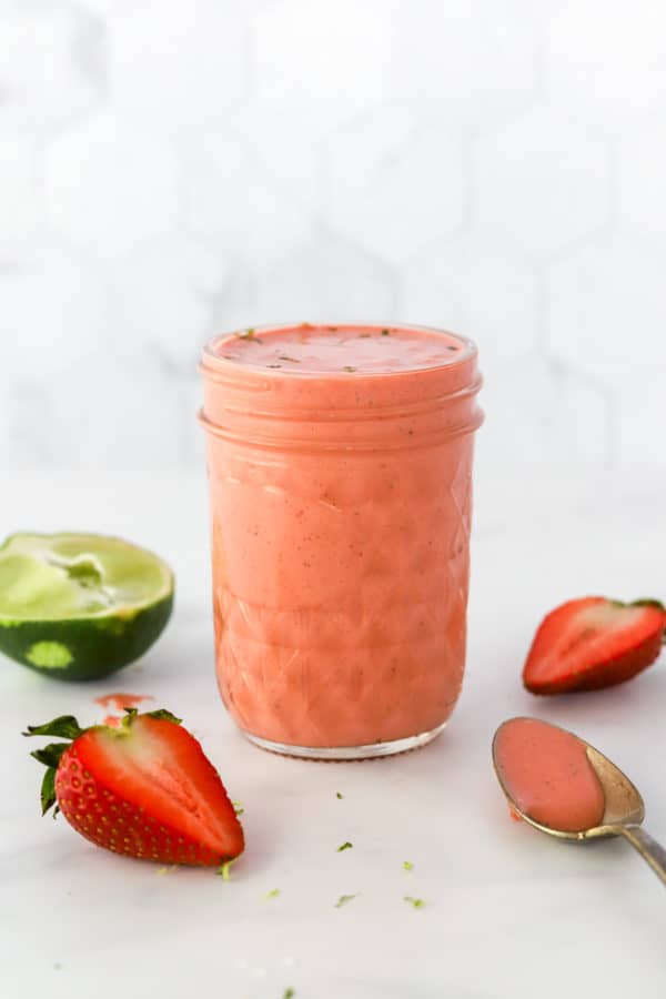 Strawberry dressing in a mason jar with sliced strawberries and a lime behind it and around it.