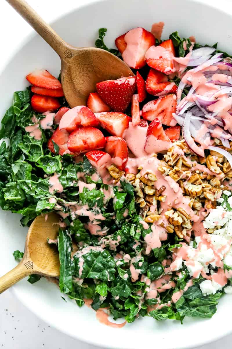 Chopped kale, sliced strawberries, sliced red onion, pecans and goat cheese in a large salad bowl topped with strawberry dressing. 