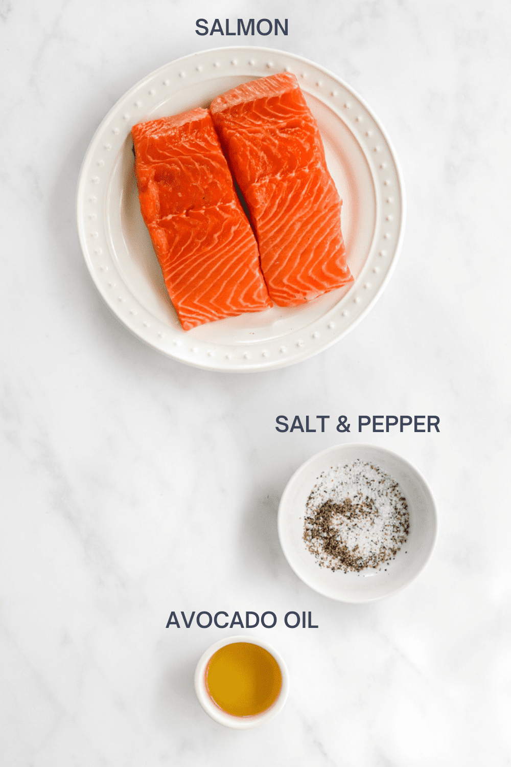 Salmon filets on a white plate with a bowl of salt and pepper and a bowl of oil in front of it with labels over each ingredient. 