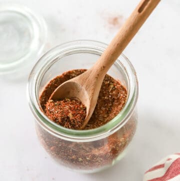 Spice blend in a glass jar with a small wooden spoon in the jar.