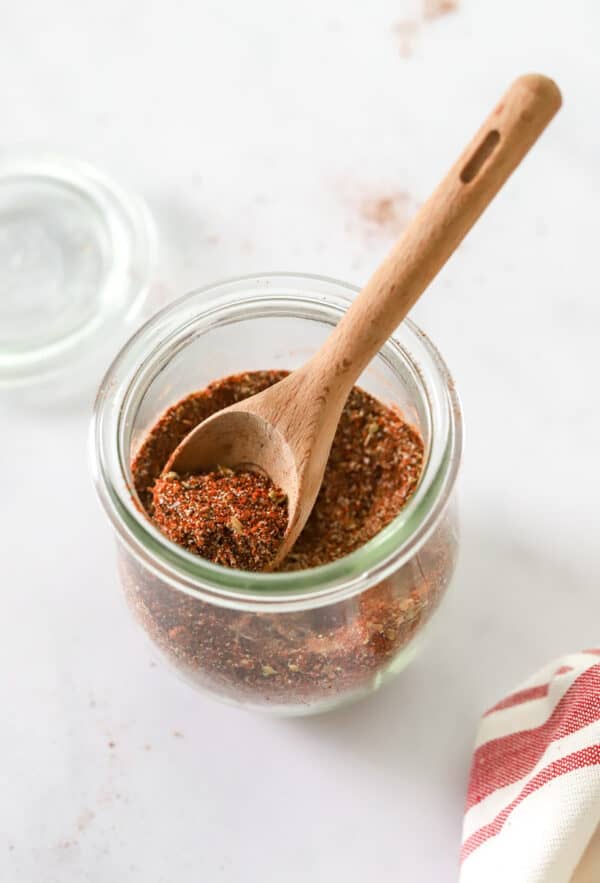 Spice blend in a glass jar with a small wooden spoon in the jar.