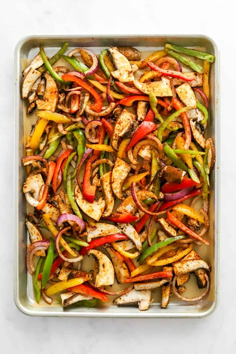 Uncooked, seasoned veggies on a sheet pan on top of brown parchment paper. 