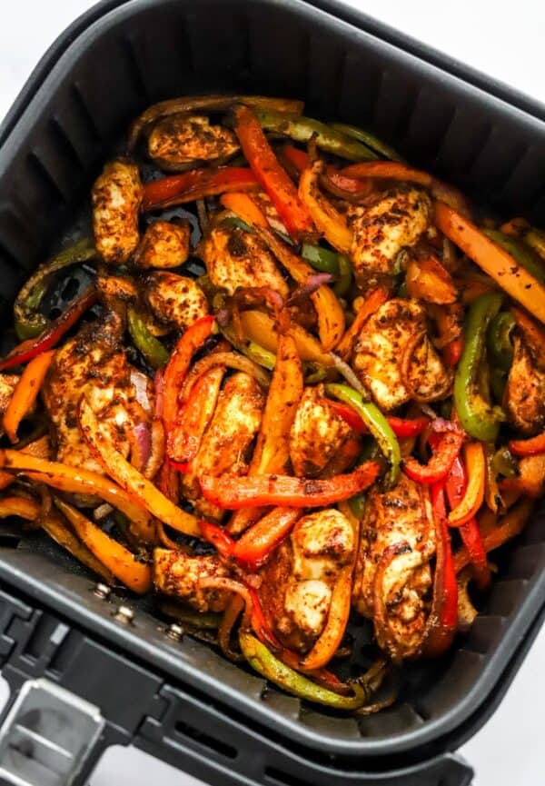 Cooked veggies and chicken in a black air fryer basket.