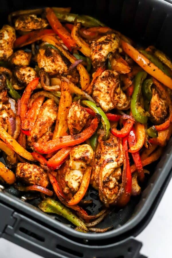Roasted chicken, onions and peppers in a black air fryer basket.