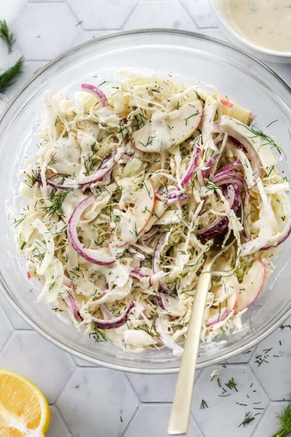 Fennel slaw with apples in a glass mixing bowl with a gold spoon in the bowl.