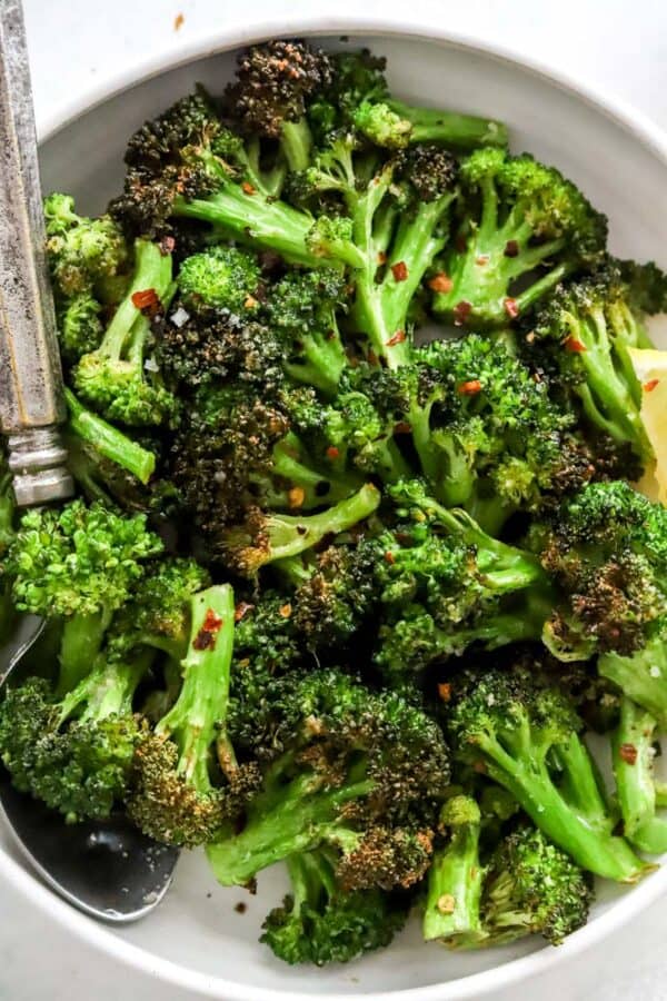 Air fryer broccoli in a bowl with a silver spoon topped with red pepper flakes.