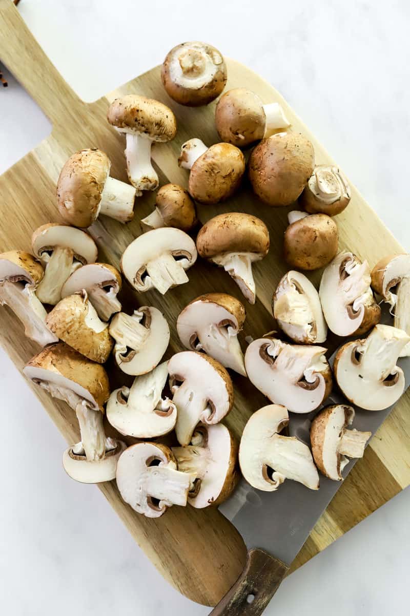 Sliced and whole mushrooms on a wooden cutting board with a silver knife on the board. 