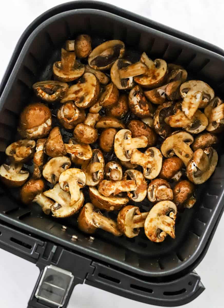 Uncooked mushrooms in a black, square air fryer basket. 