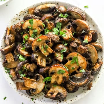 Seasoned, golden mushrooms topped with herbs on a round, white plate.