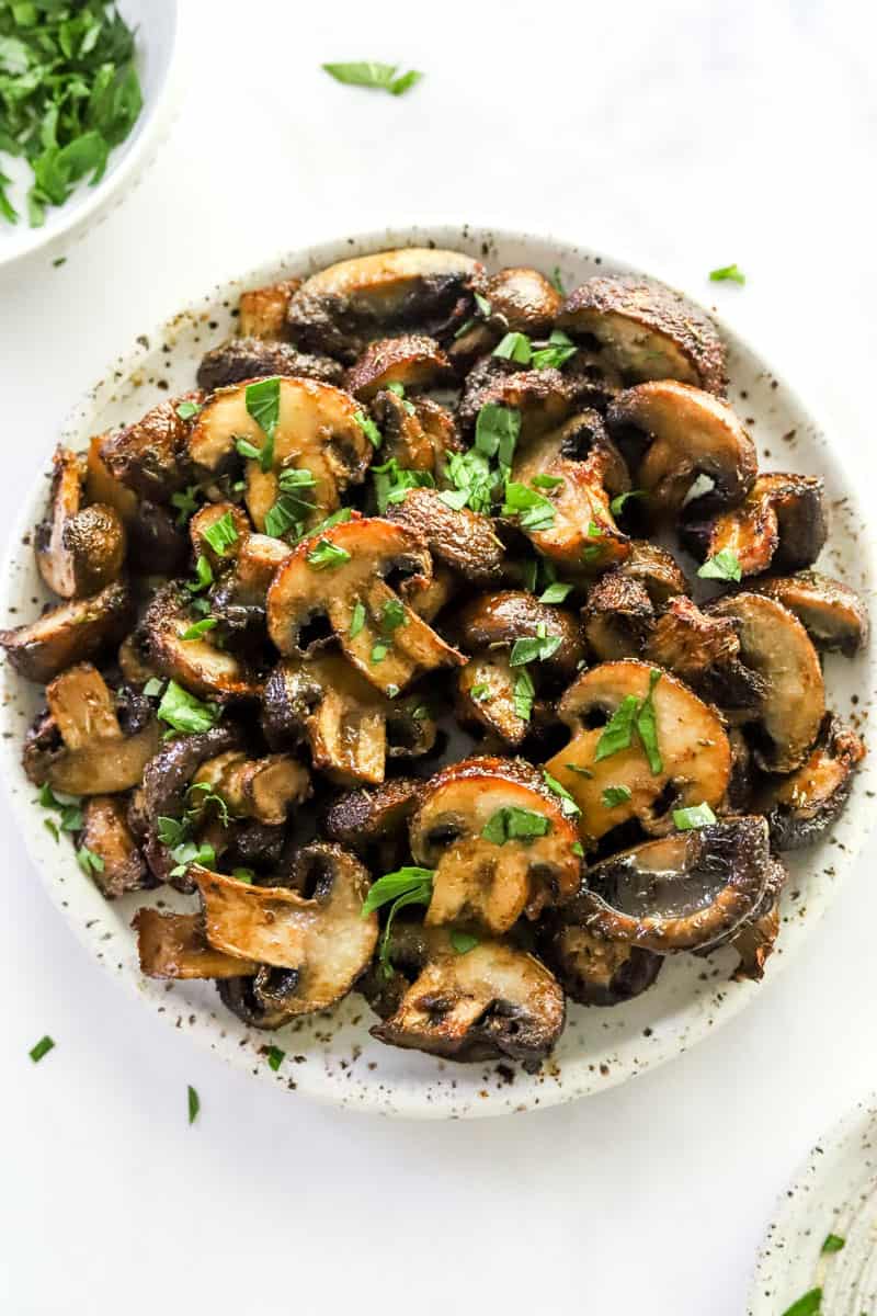 Seasoned, golden mushrooms topped with herbs on a round, white plate. 