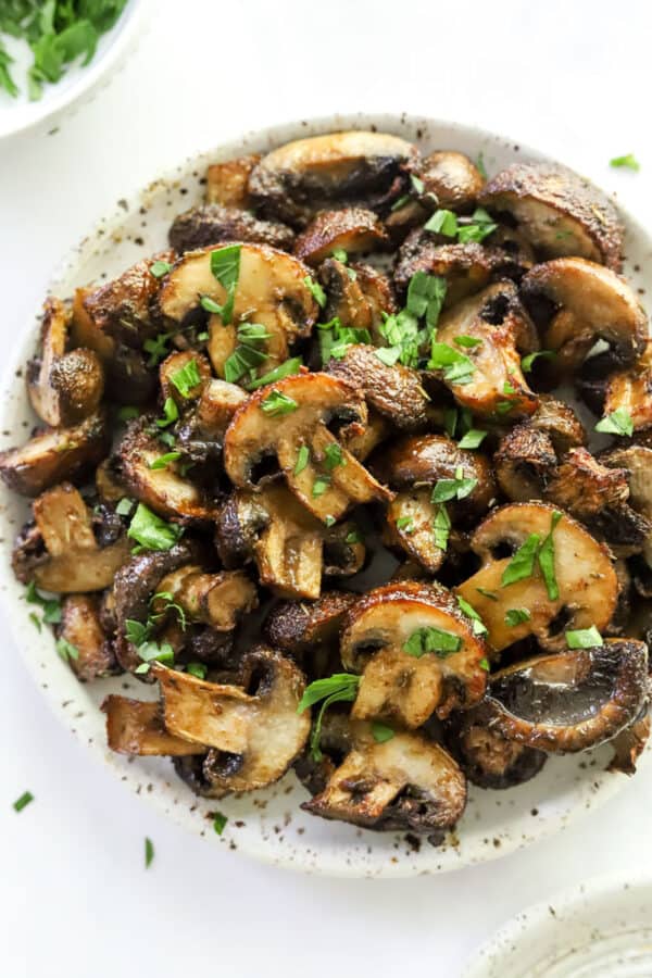Plate full of air fryer mushrooms topped with herbs.