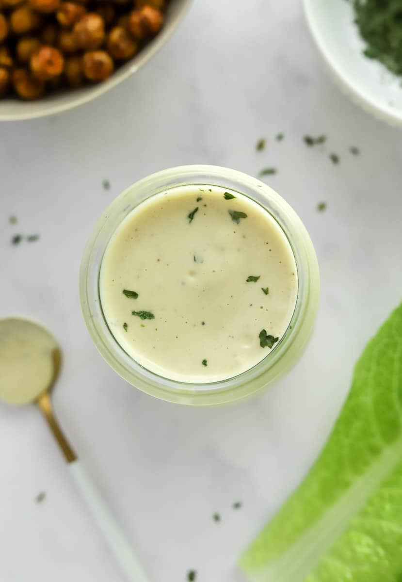 Homemade low calorie caesar dressing in a jar with a spoon next to it. 