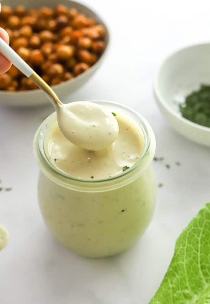 Spoon in a jar of creamy white salad dressing with a bowl of crispy chickpeas behind it.
