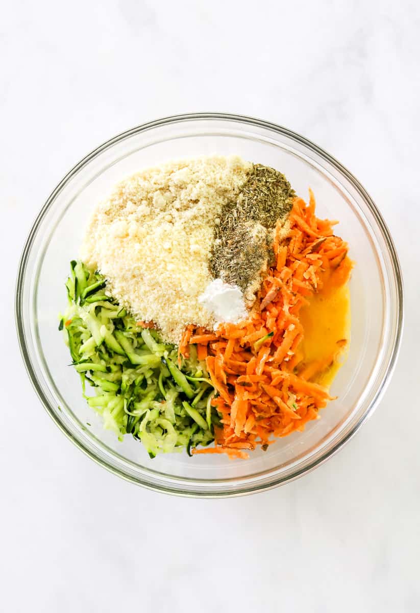Shredded green and orange veggies  with other ingredients in a glass mixing bowl. 