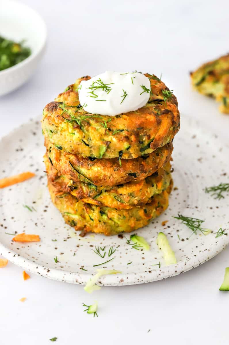 Stack of zucchini cakes with Greek yogurt and herbs on top of one of them. 