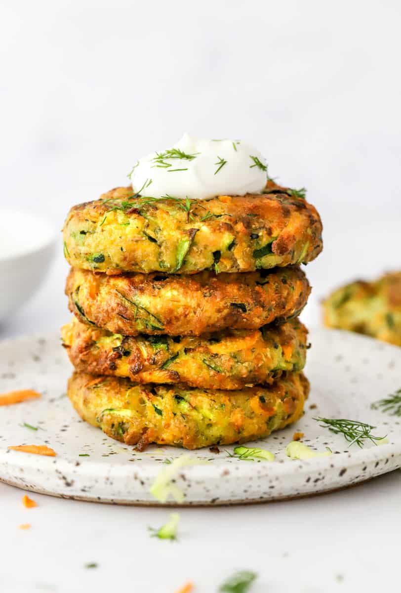 Veggies patties with zucchini and sweet potato stacked on top of one another with Greek yogurt on top sprinkle with fresh chopped dill. 