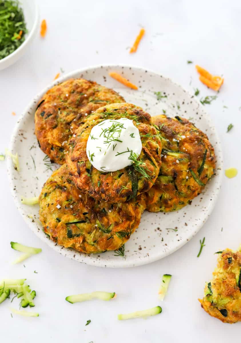 4 vegetable cakes on a plate with sour cream and herbs on top of one of the veggie cakes.