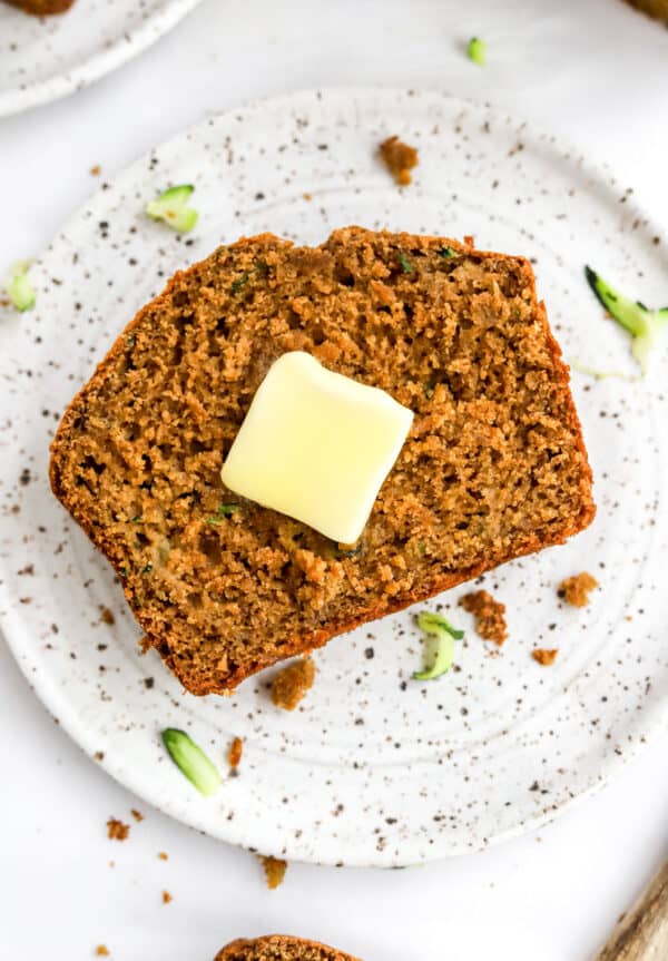 Square piece of dark brown bread with butter on it on a plate.