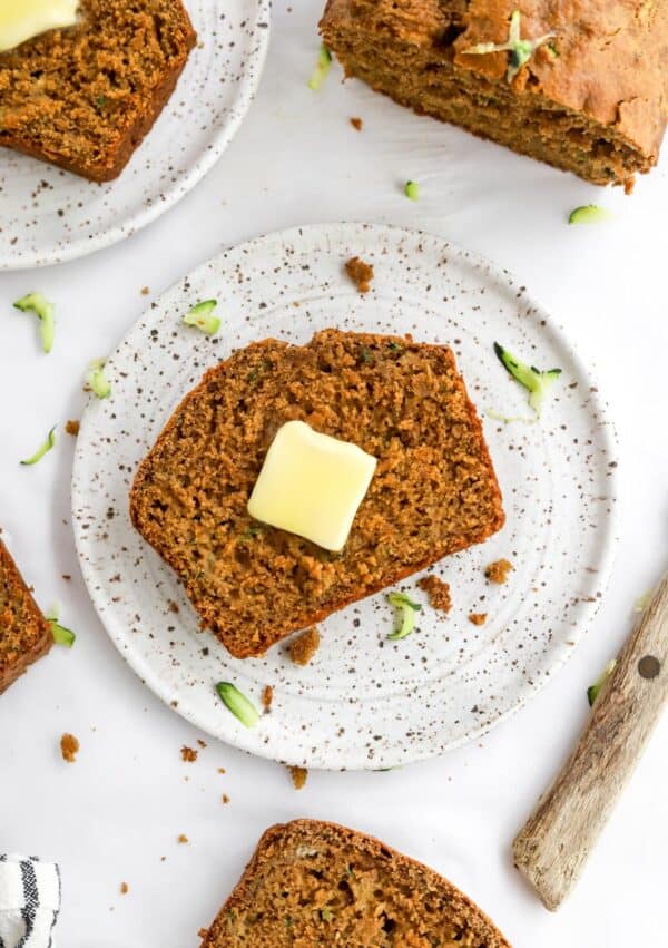 Zucchini banana bread slice on a round white plate with more sliced of bread around it.