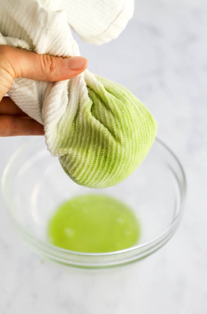 Hand wringing out water from zucchini that is wrapped up in a white kitchen towel.